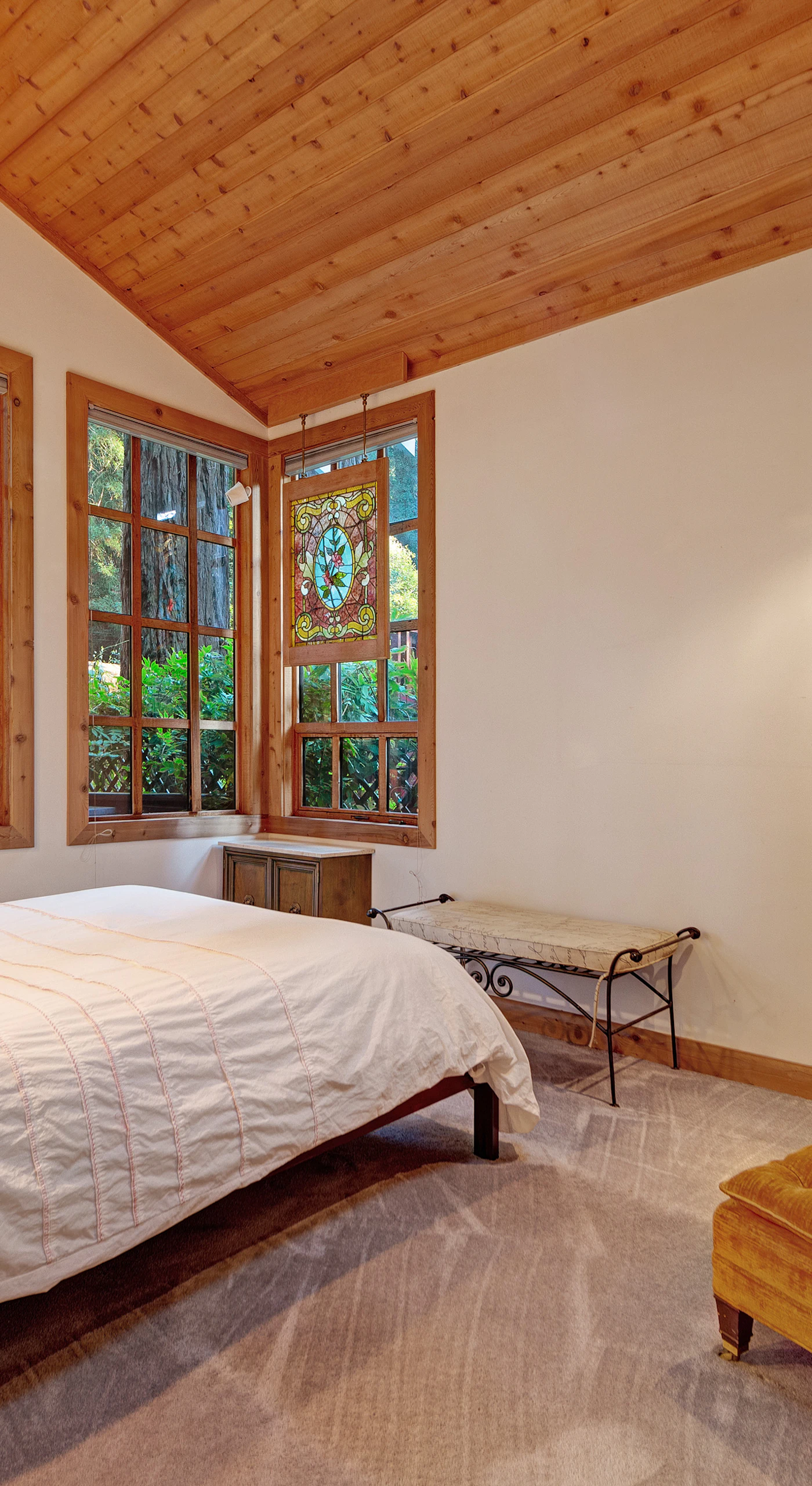 Rest peacefully in your serene bedroom with treetop views through wood-framed windows and a plush reading chair.