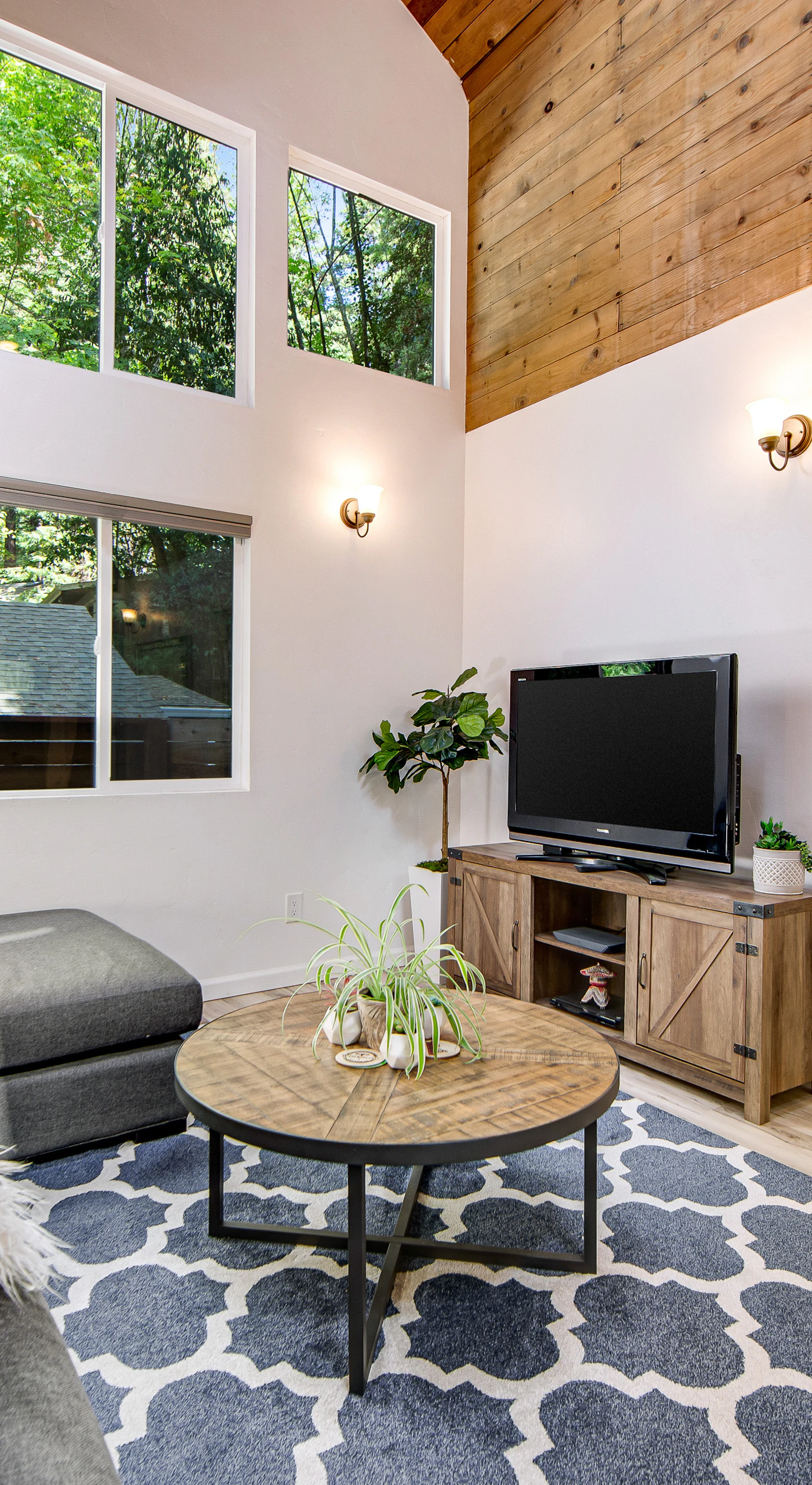 Settle into your sun-drenched living room with soaring wood-paneled ceilings, oversized windows framing the redwood canopy, and a cozy sectional for movie nights.
