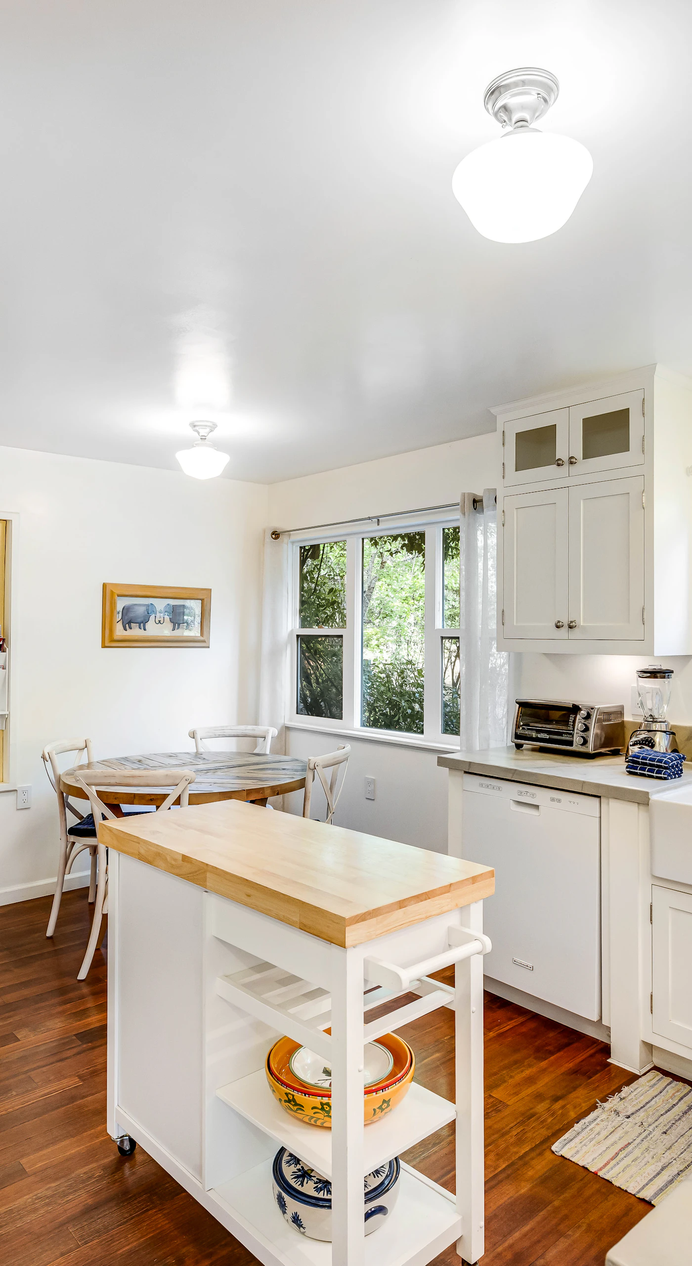 Cook with ease in your bright farmhouse kitchen featuring white cabinetry, a classic apron-front sink, and a handy rolling island