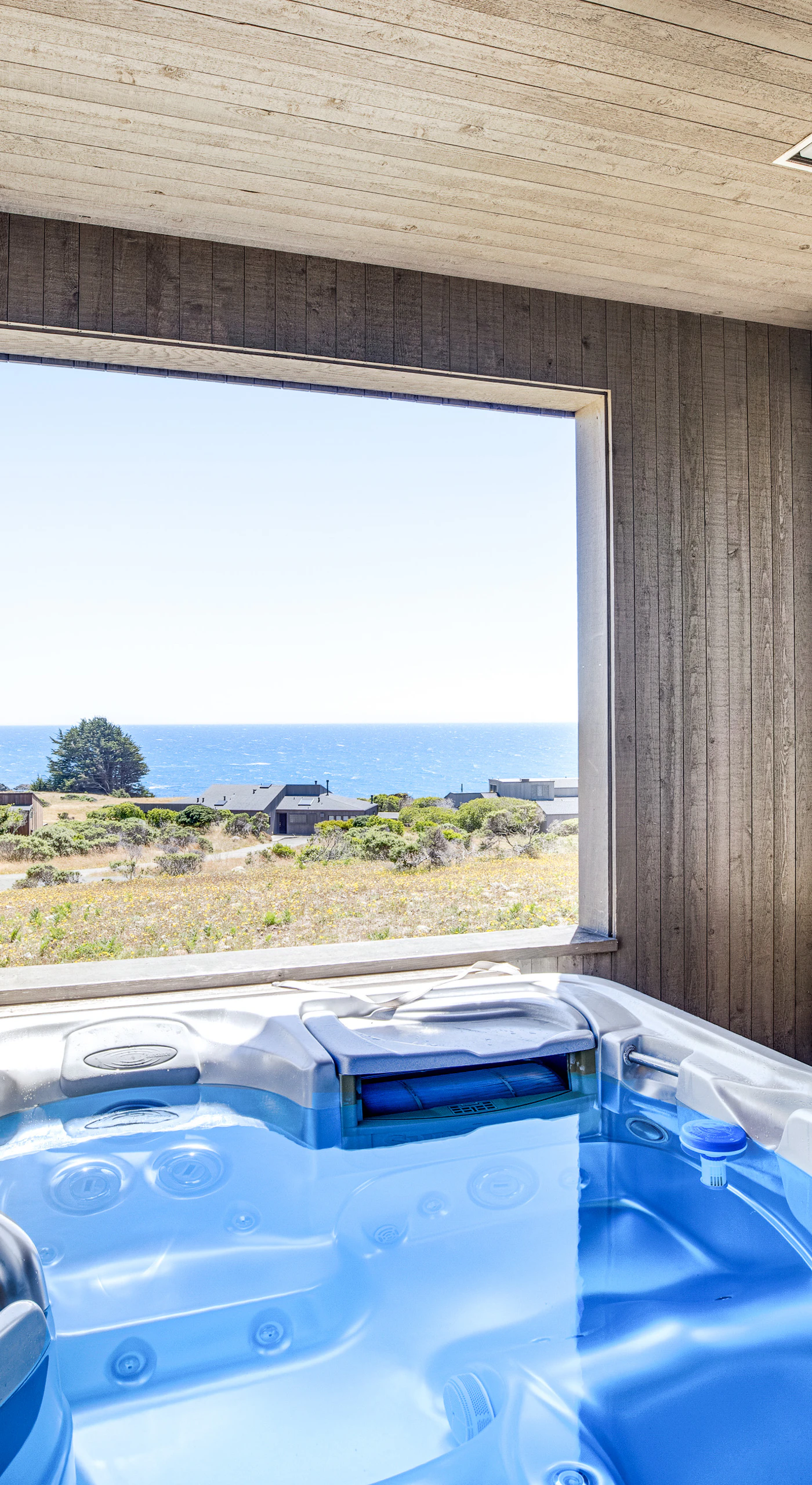 Soak in the private hot tub while enjoying stunning ocean views, the perfect way to unwind under the clear coastal skies.