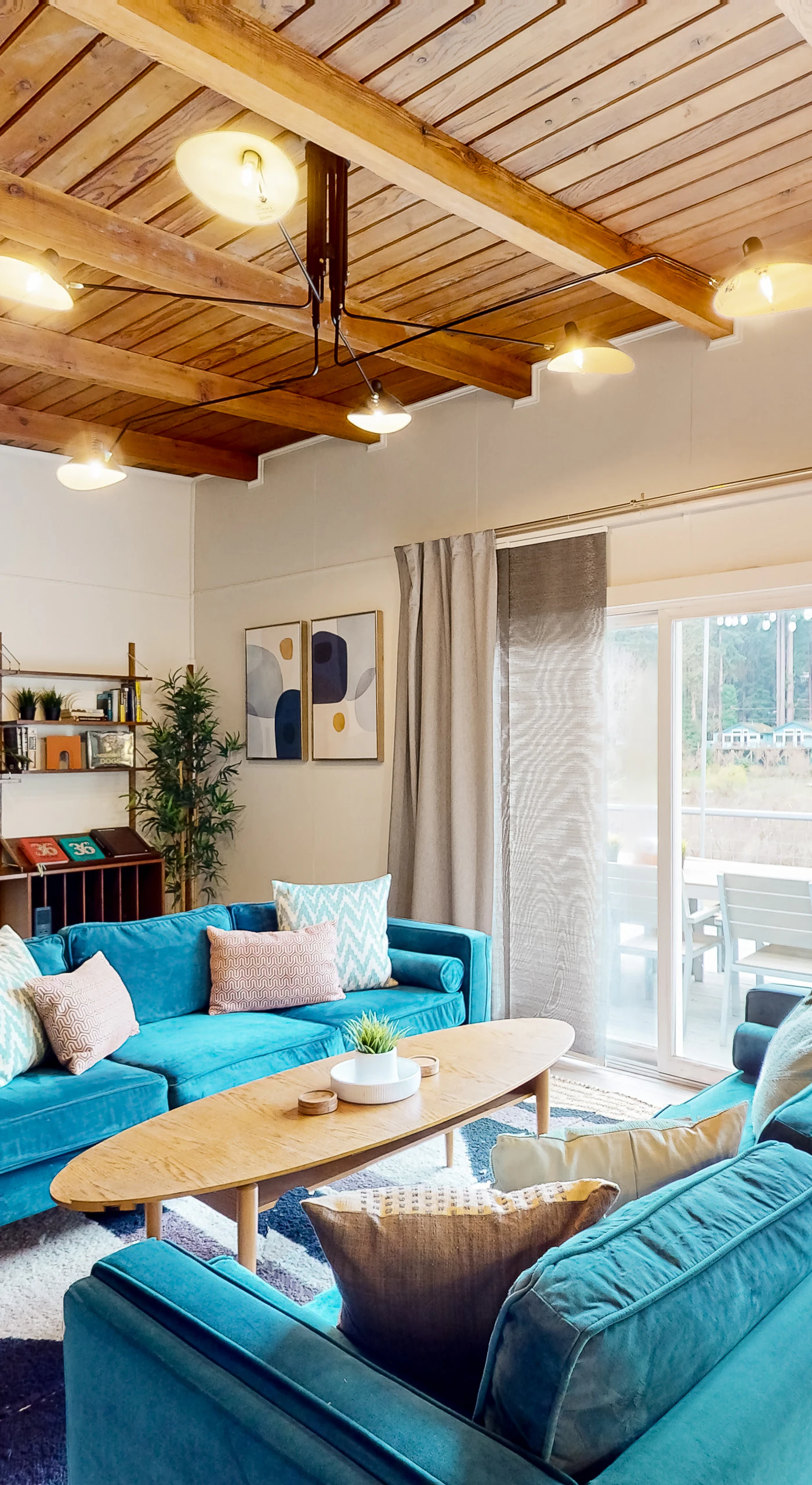 Settle into your sun-drenched living room where warm wood-beam ceilings and vibrant teal sofas invite you to relax after a day exploring Russian River wine country.