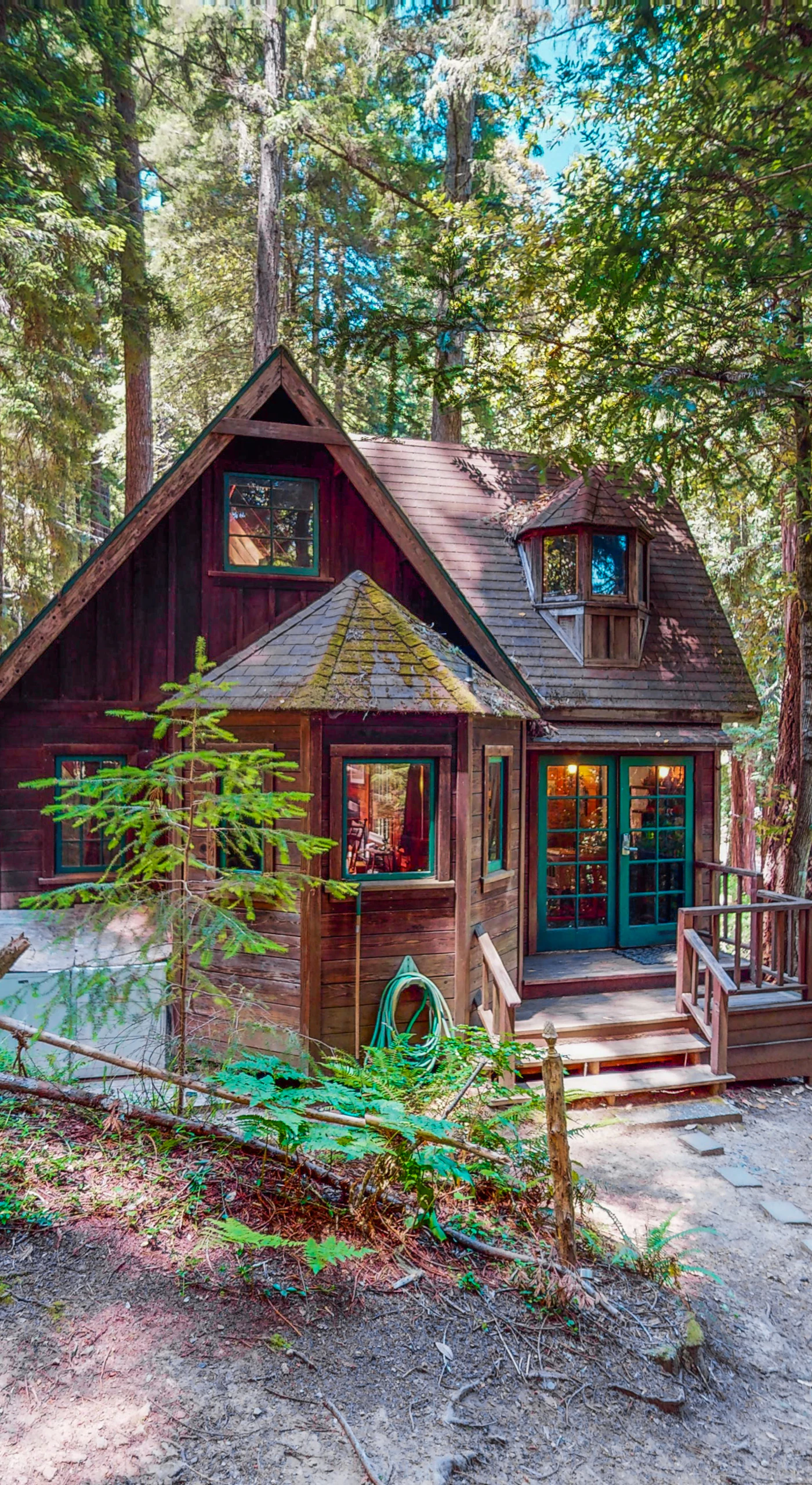 Tucked beneath towering Cazadero redwoods, your storybook cottage awaits — whimsical A-frame charm, warm wood siding, and a stone pathway leading to your private forest hideaway.