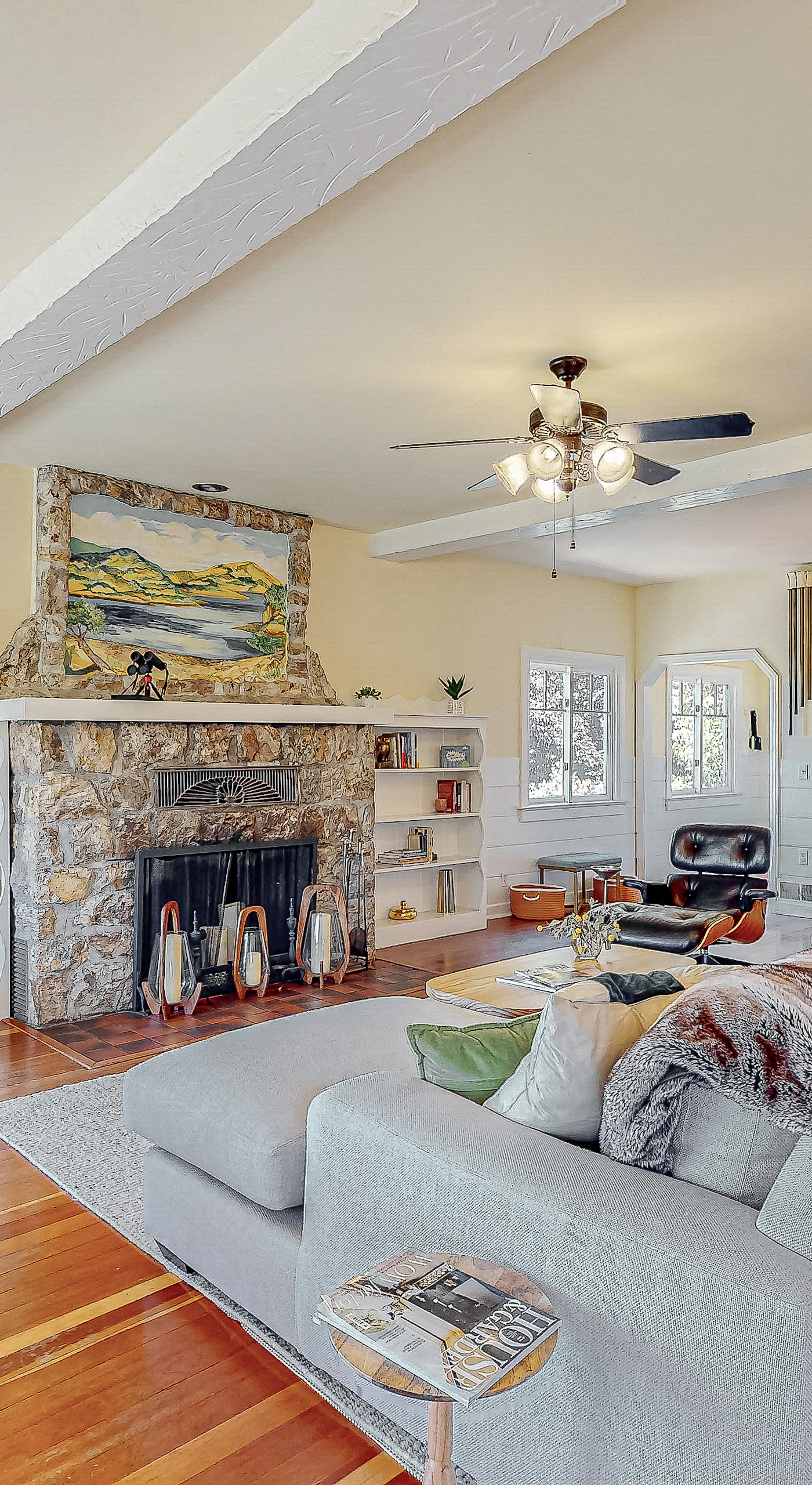 Sink into the sofa beside a striking stone fireplace in your Healdsburg cottage living room — hardwood floors, built-in shelves, and a ceiling fan keep every wine country evening comfortable.