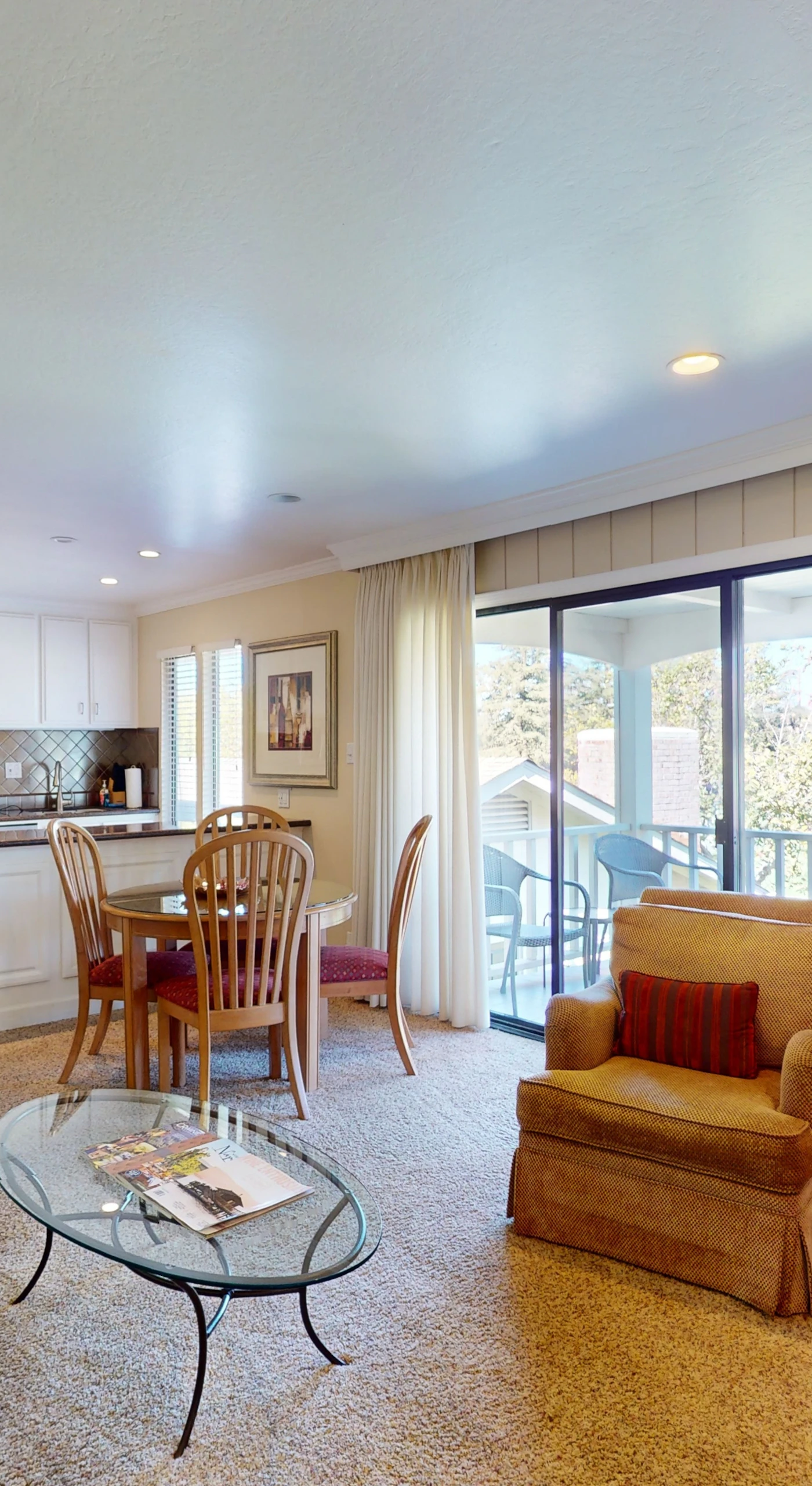 Step into your sunlit Napa Valley retreat — an open-concept living space with kitchenette, cozy seating, and sliding glass doors framing your private balcony view.