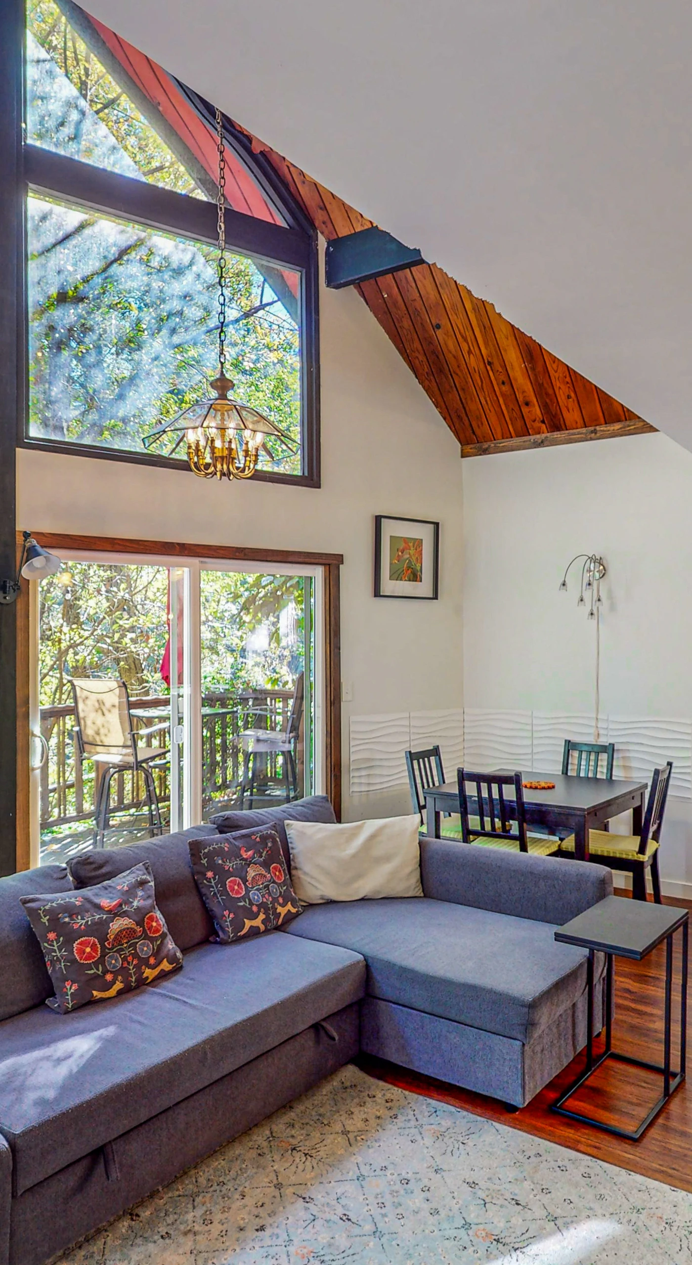 Sunlight floods your vaulted A-frame living room through soaring windows — sink into the sectional and watch redwood canopy sway just beyond the deck.