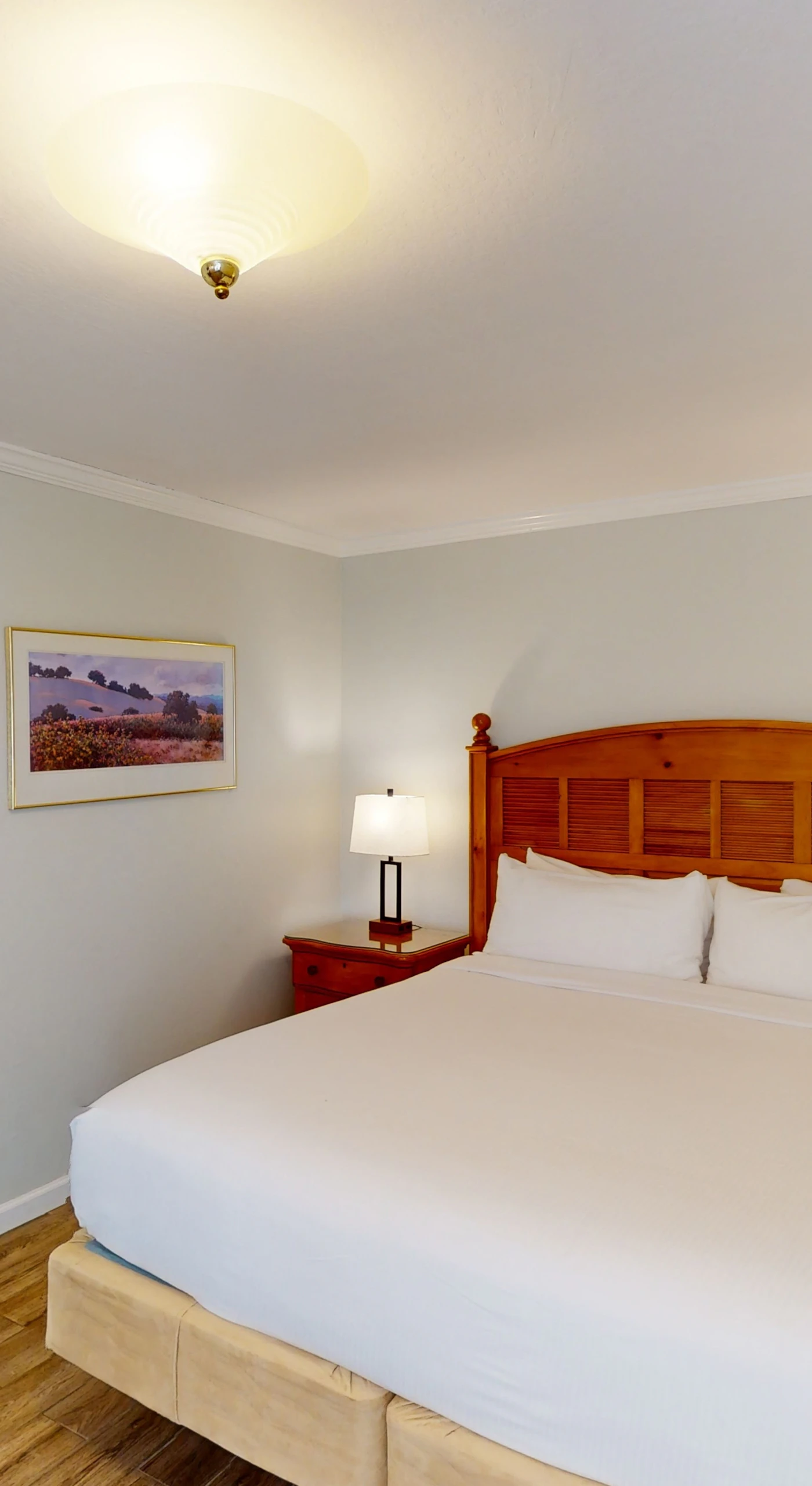 Sink into your plush king bed after a day exploring Napa Valley wineries — crisp white linens and warm wood furnishings set a restful wine country tone.