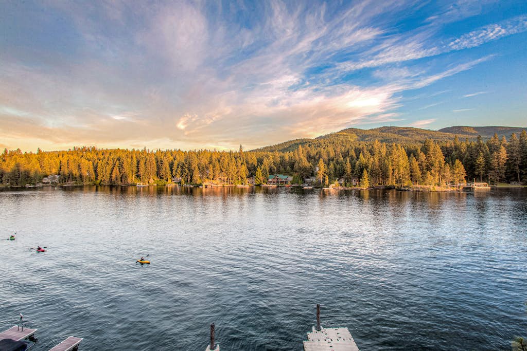 North Idaho's premier riverside lodge for large groups—4 bedrooms, 4 bathrooms, private Spokane River dock with boat slip, sauna, game room, and 93 feet of private river frontage. The home that delivers the full lodge experience: timber beams, stone fireplace, chef's kitchen, and river views from nearly every window. Built for groups who take their downtime seriously.