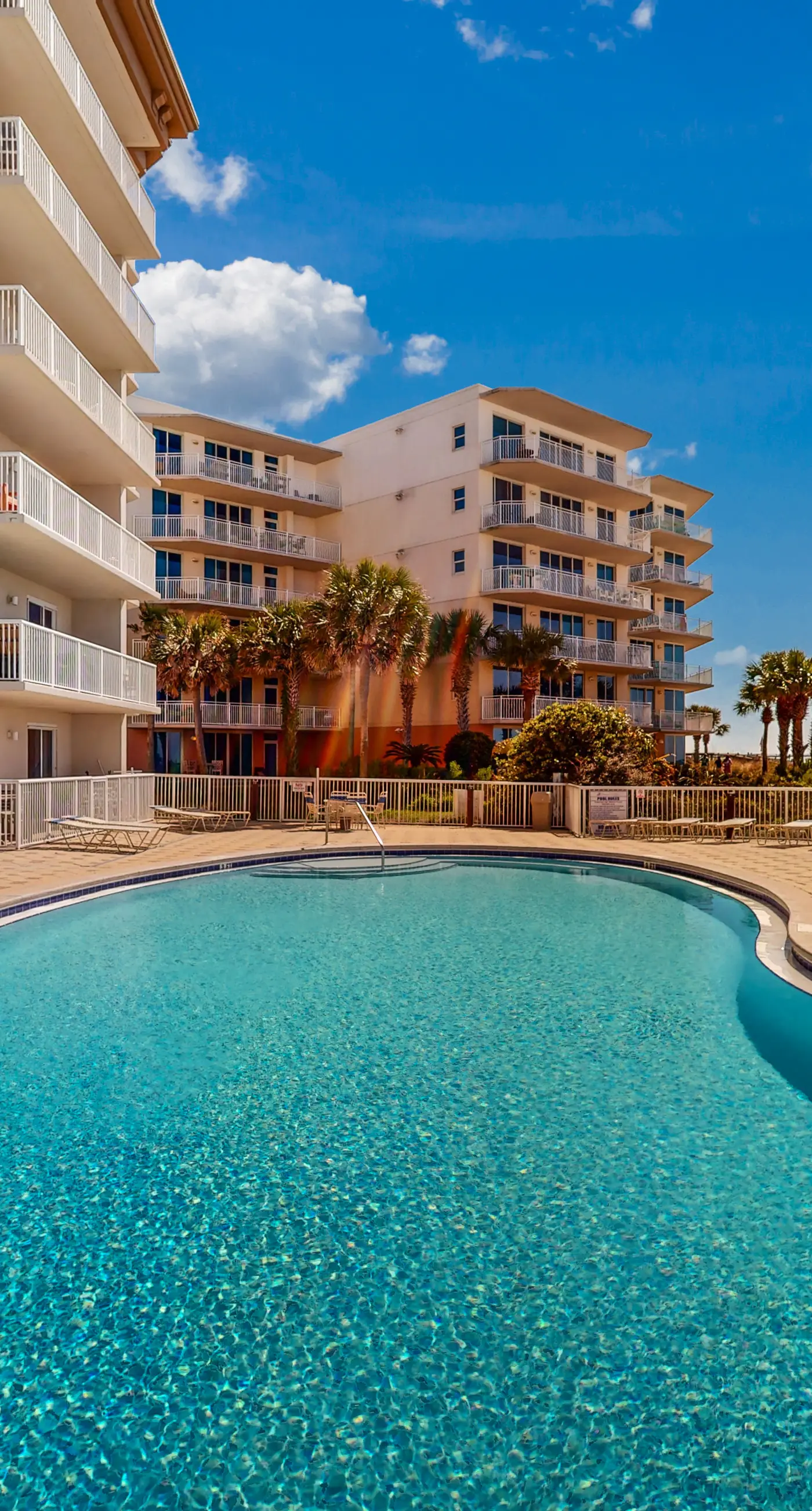 Beachfront condo with beach chairs, an umbrella, and a pool