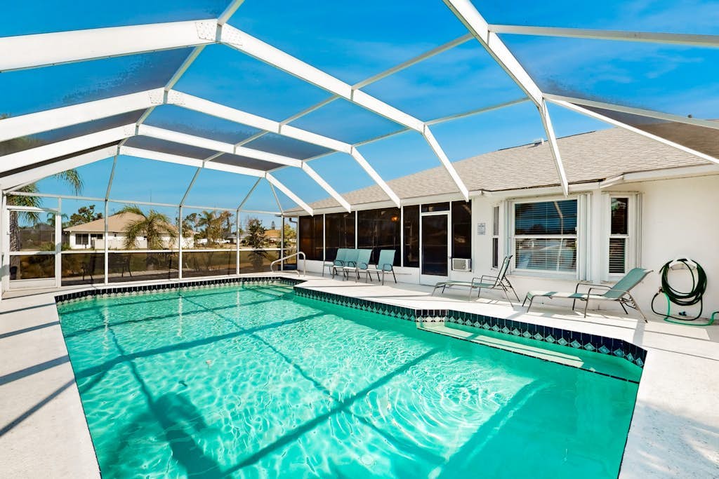 Palm-lined waterfront retreat with enclosed pool, inviting patio, & central AC