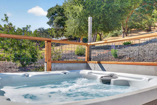 Sunlight pours through floor-to-ceiling windows as hillside oaks frame your view of the Sonoma Valley. This contemporary four-bedroom retreat pairs designer interiors — navy accents, gold fixtures, a linear fireplace — with a private hot tub set among lavender and native grasses. Glen Ellen Star is 0.4 miles away and Jack London State Historic Park just one mile from your door. Soak under the stars, wake to mountain views, and let the valley do the rest.
