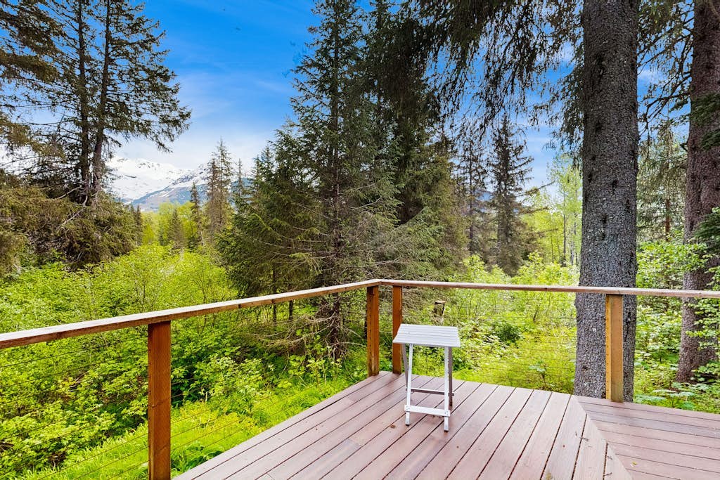 A modern cabin that proves contemporary lines and Girdwood’s deep woods don't have to fight. Tucked into a quiet, secluded pocket of trees a mile and a half from Alyeska Resort, this retreat trades the bustle of the village center for absolute mountain privacy. The architecture boasts towering ceilings, modern upscale furnishings, a custom spiral staircase climbing to a private loft bedroom, and a massive outdoor deck pointed at the peaks. Walk to Girdwood Brewing Company or Chair 5 Restaurant, and bring the dog along—they are completely welcome here. *4WD/traction tires strictly required in winter.* Standard Specs: Fully equipped kitchen, private mountain-view deck, flat-screen TV, high-speed WiFi, and keypad entry. Driveway parking for two vehicles. Dog-friendly. Sleeps 6.