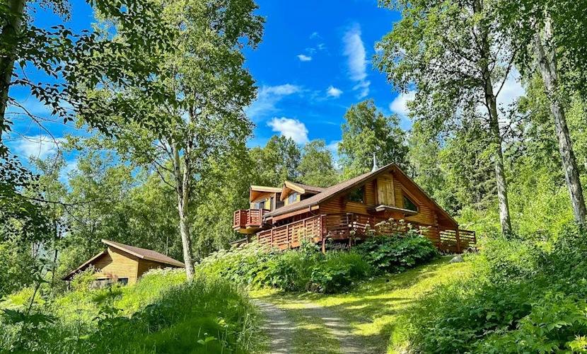 The cabin sits exactly where the road runs out—thirty minutes outside of Anchorage and fifteen minutes from downtown Eagle River, completely embedded inside a rugged wilderness where moose move through the yard and the northern lights handle the winter sky. Constructed with traditional log walls and framing picture windows, the home features a classic wood stove, a master bedroom loft with an en-suite bath, and a large viewing deck. Engineered for remote professionals, the cabin includes dedicated high-speed WiFi and a workspace docking station packed with two desktop monitors. Located two miles from the Eagle River Nature Center trail loops and salmon-viewing deck. *Winter notice: 4WD strictly required.* Standard Specs: Fully equipped kitchen with dishwasher, wood stove, executive desk workspace with dual monitors, viewing deck, private laundry, high-speed WiFi, and safety tools. Driveway parking for three vehicles (steep loop). Dog-friendly. No parties/strict quiet hours. Sleeps 6.